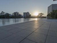 a fountain in the middle of a public park at sunrise time with the sun setting over buildings