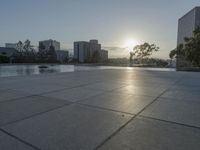 a fountain in the middle of a public park at sunrise time with the sun setting over buildings