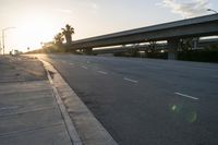 the sun rising behind the freeway bridge on an empty street in front of palm trees