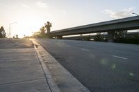 the sun rising behind the freeway bridge on an empty street in front of palm trees