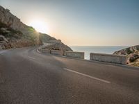 a empty road with some cliffs on either side and the ocean in the background, with a blue sky