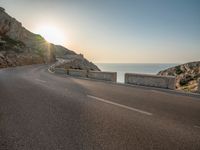 a empty road with some cliffs on either side and the ocean in the background, with a blue sky