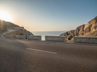 a empty road with some cliffs on either side and the ocean in the background, with a blue sky