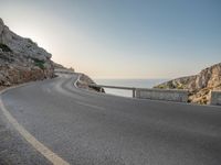 a empty road with some cliffs on either side and the ocean in the background, with a blue sky