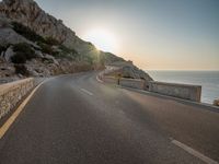 a empty road with some cliffs on either side and the ocean in the background, with a blue sky