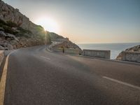 a empty road with some cliffs on either side and the ocean in the background, with a blue sky