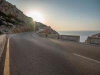 a empty road with some cliffs on either side and the ocean in the background, with a blue sky