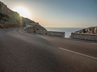 a empty road with some cliffs on either side and the ocean in the background, with a blue sky