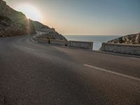 a empty road with some cliffs on either side and the ocean in the background, with a blue sky