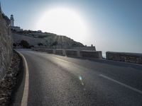 a motorcycle riding down an empty road next to a cliff on a sunny day in summer