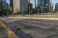 a deserted street is next to a city skyline with tall buildings in the distance and a fence is on the opposite side