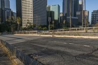 a deserted street is next to a city skyline with tall buildings in the distance and a fence is on the opposite side