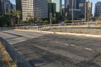 a deserted street is next to a city skyline with tall buildings in the distance and a fence is on the opposite side