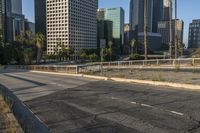 a deserted street is next to a city skyline with tall buildings in the distance and a fence is on the opposite side