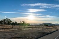 the road is empty in the open space as the sun sets over a hilly area