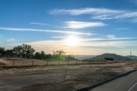 the road is empty in the open space as the sun sets over a hilly area