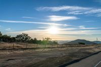 the road is empty in the open space as the sun sets over a hilly area