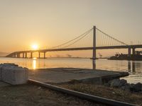 a very big bridge over the water with some boats in it by the shore with the sun rising through the window