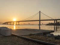 a very big bridge over the water with some boats in it by the shore with the sun rising through the window