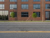 an empty street in front of a large red brick building on the other side of the road is a street light that has a line for motorists