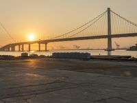 the view of a bridge in the distance near water and sand at sunset time, with the sun shining through the windows