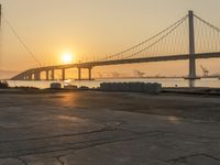 the view of a bridge in the distance near water and sand at sunset time, with the sun shining through the windows