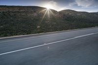 the sun is rising on a road surrounded by mountains and trees on the side of the road