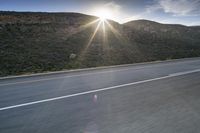 the sun is rising on a road surrounded by mountains and trees on the side of the road