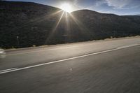 the sun is rising on a road surrounded by mountains and trees on the side of the road