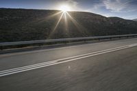 the sun is rising on a road surrounded by mountains and trees on the side of the road