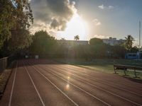 a sunrise at a track and field with some benches near it and a fence with the sun rising in the background