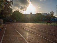 a sunrise at a track and field with some benches near it and a fence with the sun rising in the background