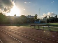 a sunrise at a track and field with some benches near it and a fence with the sun rising in the background