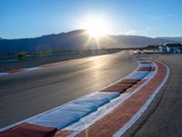 a photo of a dirt race track with sun setting in the distance of the track