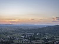 a cloudy sky above the town and the hills and the sun is setting above it