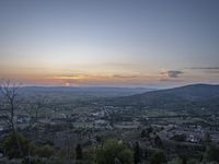 a cloudy sky above the town and the hills and the sun is setting above it