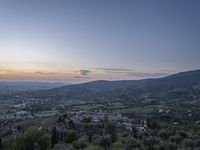 a cloudy sky above the town and the hills and the sun is setting above it