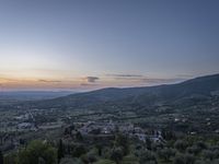 a cloudy sky above the town and the hills and the sun is setting above it