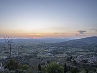 a cloudy sky above the town and the hills and the sun is setting above it