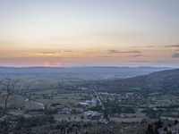 a cloudy sky above the town and the hills and the sun is setting above it