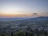 a cloudy sky above the town and the hills and the sun is setting above it