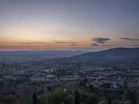 a cloudy sky above the town and the hills and the sun is setting above it