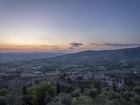 a cloudy sky above the town and the hills and the sun is setting above it