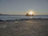 the sun sets over a rocky outcropping in the ocean at low tide