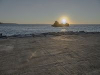 the sun sets over a rocky outcropping in the ocean at low tide