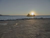 the sun sets over a rocky outcropping in the ocean at low tide