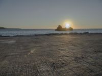 the sun sets over a rocky outcropping in the ocean at low tide