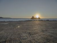 the sun sets over a rocky outcropping in the ocean at low tide