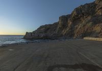 a beautiful beach next to a large cliff by the ocean at sunset time as seen from below