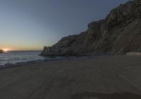 a beautiful beach next to a large cliff by the ocean at sunset time as seen from below